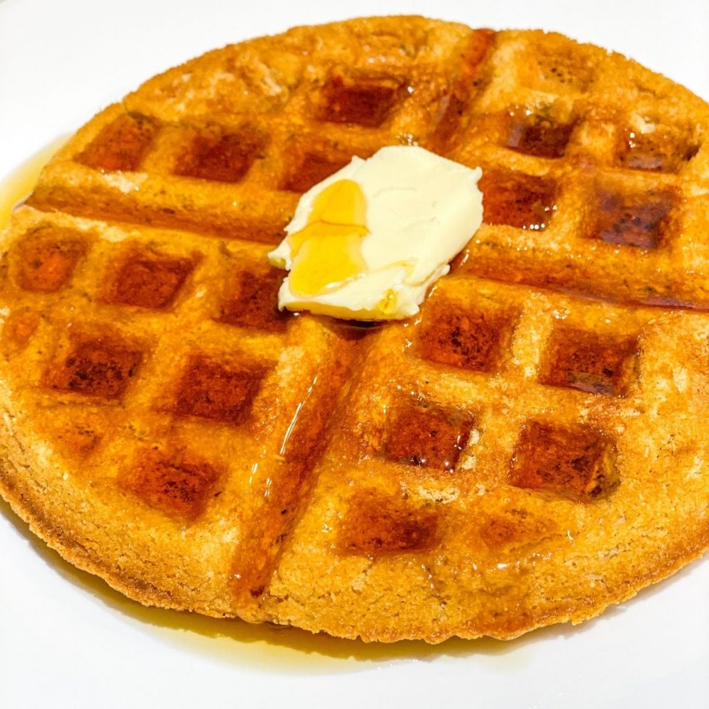 waffle on a white plate with butter and syrup.